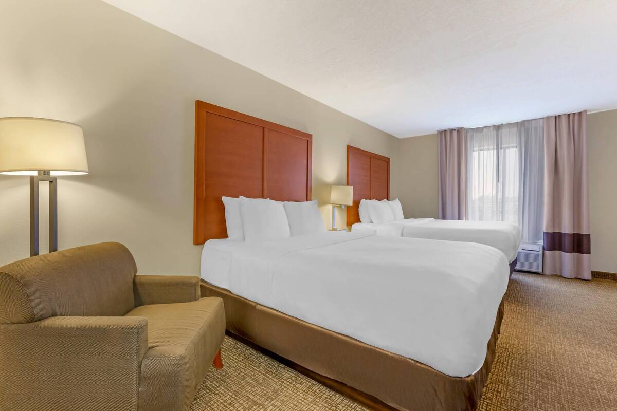 A hotel room with two beds, a sofa, a lamp, and a large window with curtains.