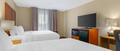 A hotel room with two beds, a television, a desk with a lamp, and a window with curtains.