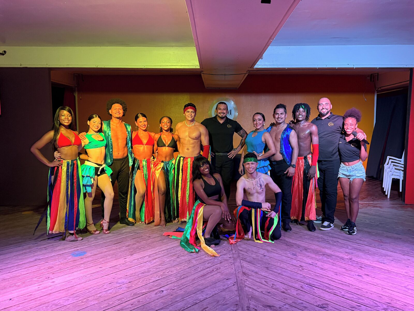 A group of people on a wooden floor with a stage area in the background.