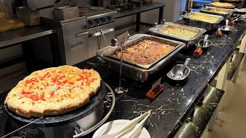 A buffet setup with various food items and a pizza on a grill.