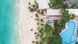 An aerial view of a beachside resort with a swimming pool, palm trees, and beach chairs. - Henry Morgan Resort - All Inclusive (Roatan)