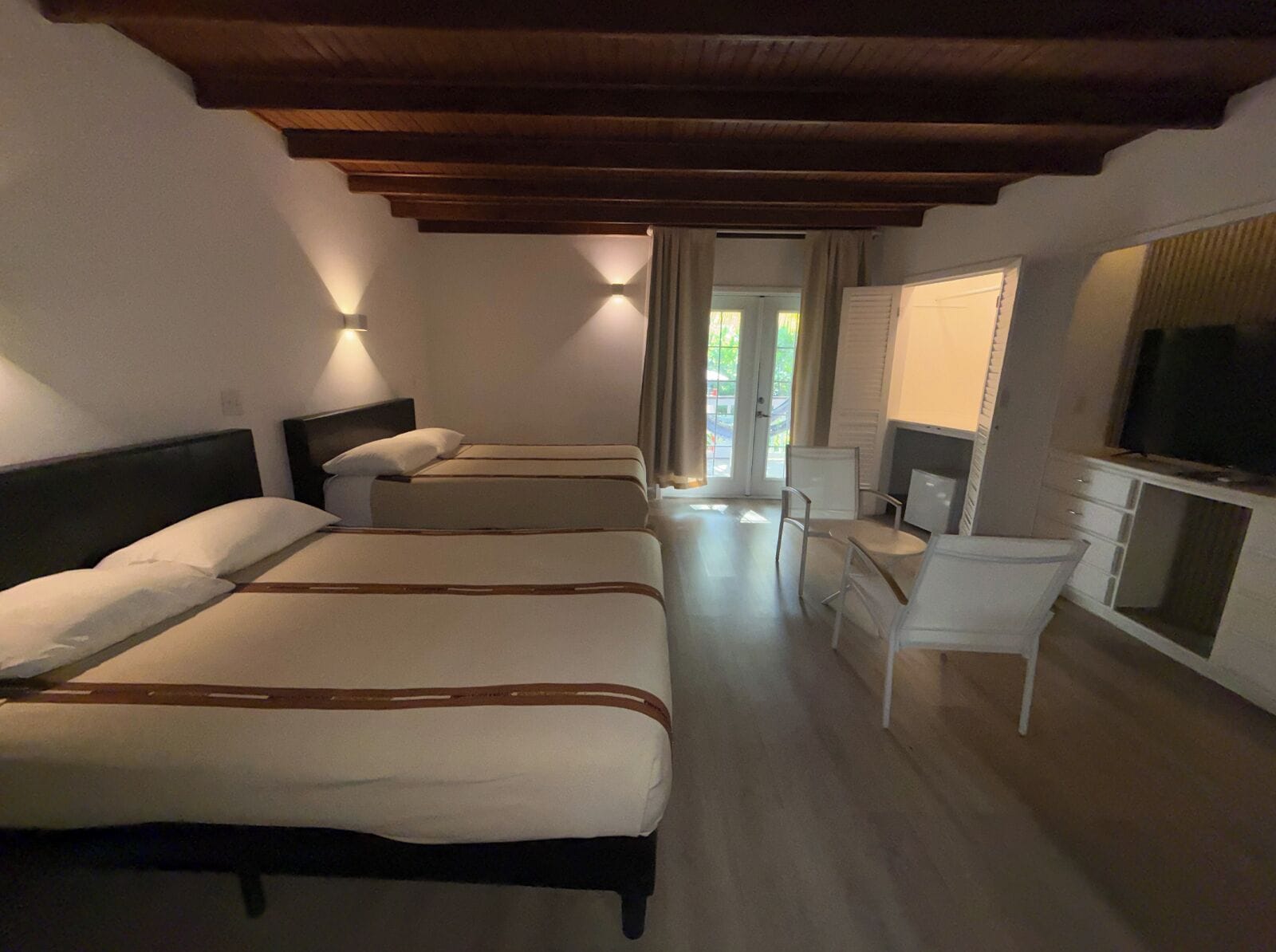 Una habitación de hotel con cuatro camas, un escritorio, una silla, un televisor y vistas al exterior.