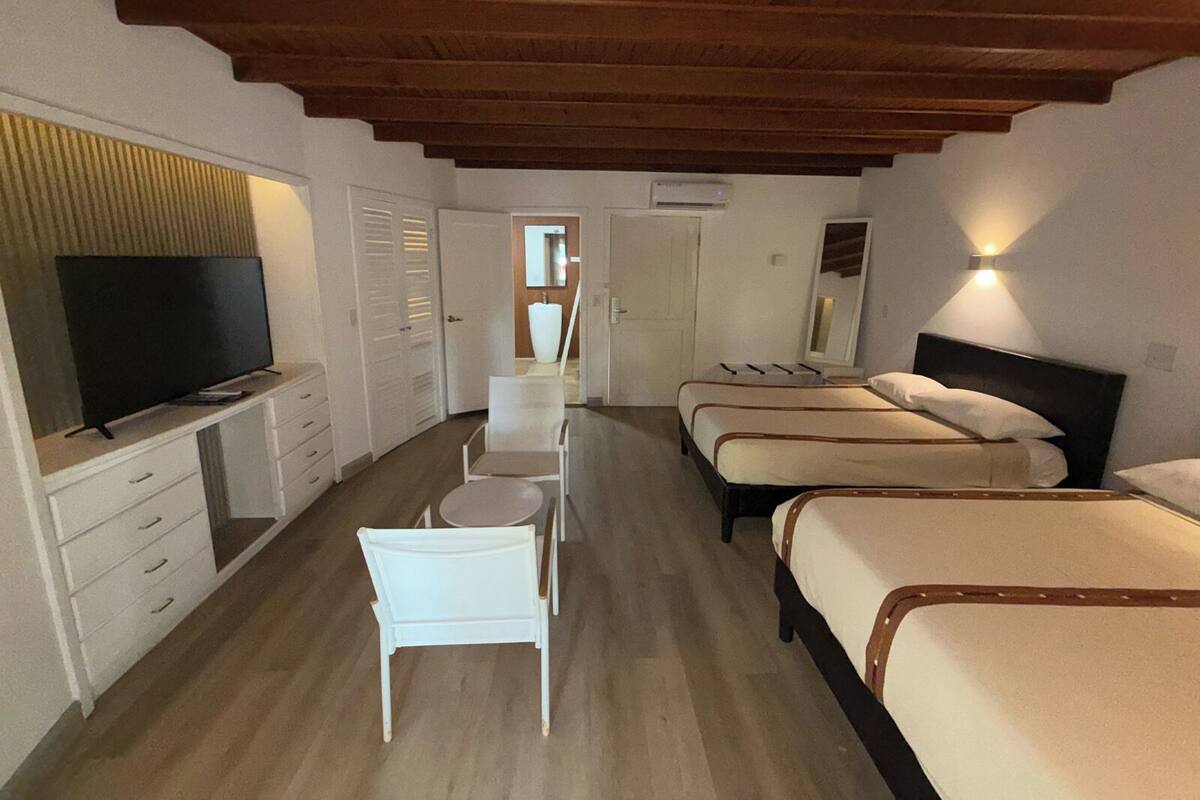 A bedroom with two beds, a TV, a desk with drawers, and a chair.