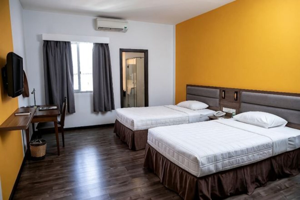 A hotel room with two beds, a desk, a chair, a TV, and a window with curtains.