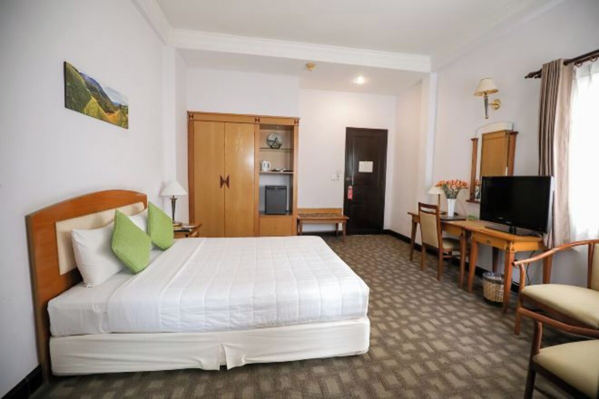 A hotel room with a bed, a desk, a television, and a wardrobe.
