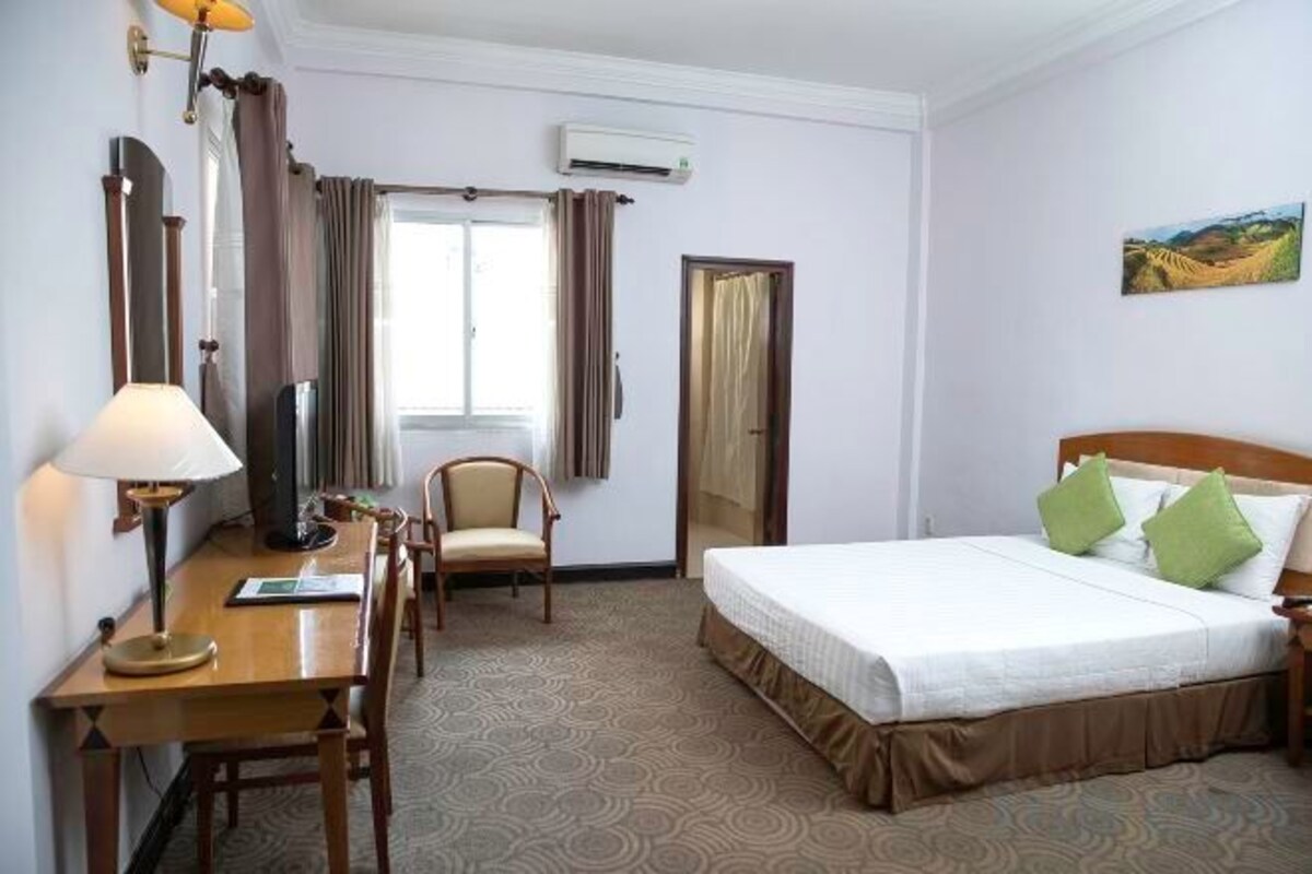 Una habitación de hotel con cama, escritorio, silla, televisión y aire acondicionado.