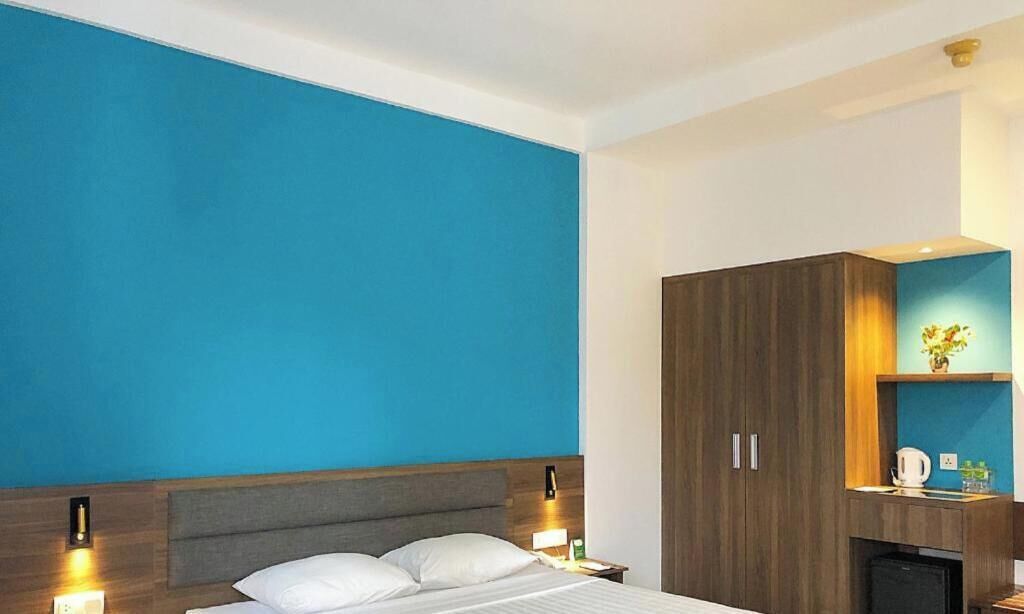 A hotel room with a large bed, a wardrobe, and a small kitchenette area.
