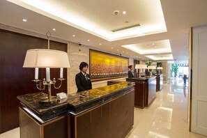 A hotel reception area with a marble counter, a large abstract painting on the wall, and a receptionist. - Metropolo Shanghai Minhang Hotel (Shanghai)
