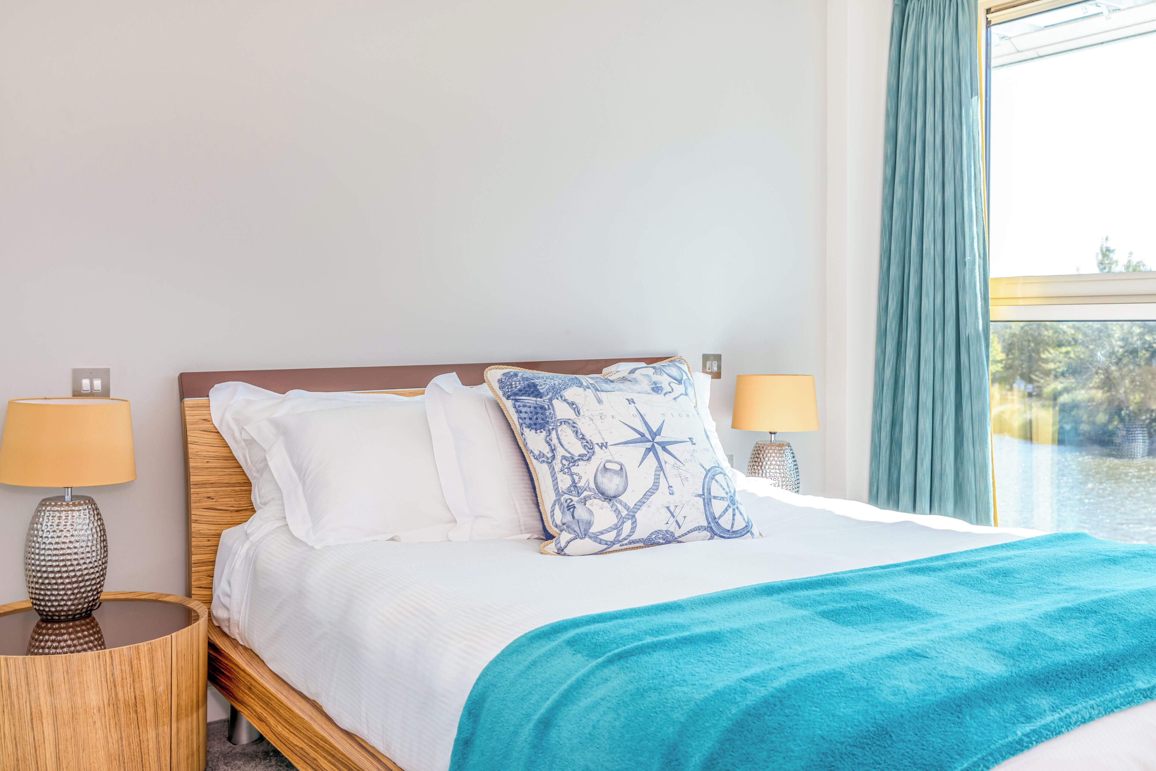 A neatly made bed with white linens and a blue patterned pillow, flanked by two bedside lamps on wooden nightstands.