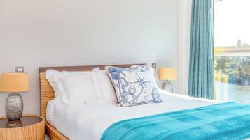 A neatly made bed with white linens and a blue patterned pillow, flanked by two bedside lamps on wooden nightstands.