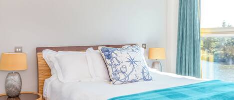 A neatly made bed with white linens and a blue patterned pillow, flanked by two bedside lamps on wooden nightstands.
