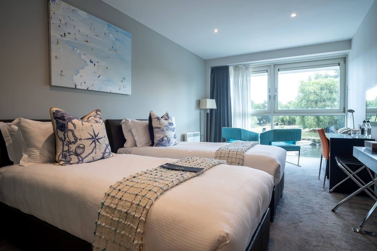 A hotel room with two beds, a desk, a chair, and a large window with a view.