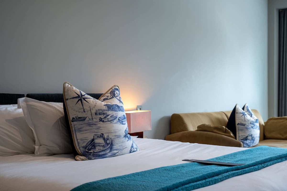 A neatly made bed with a blue and white patterned pillow, a teal throw blanket, and a wooden headboard.