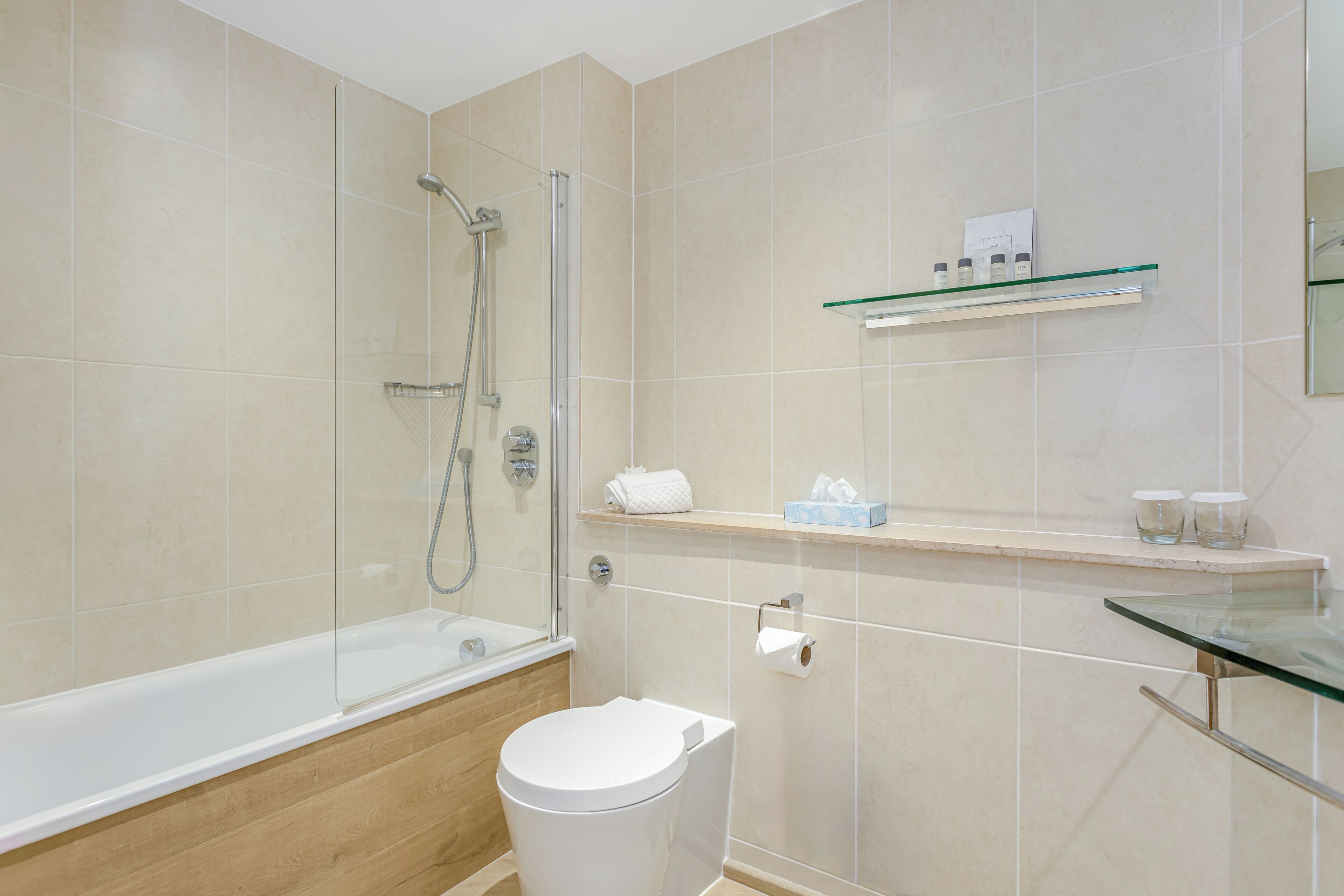 Un baño moderno con ducha de vidrio, inodoro blanco y repisa de vidrio con artículos de aseo.