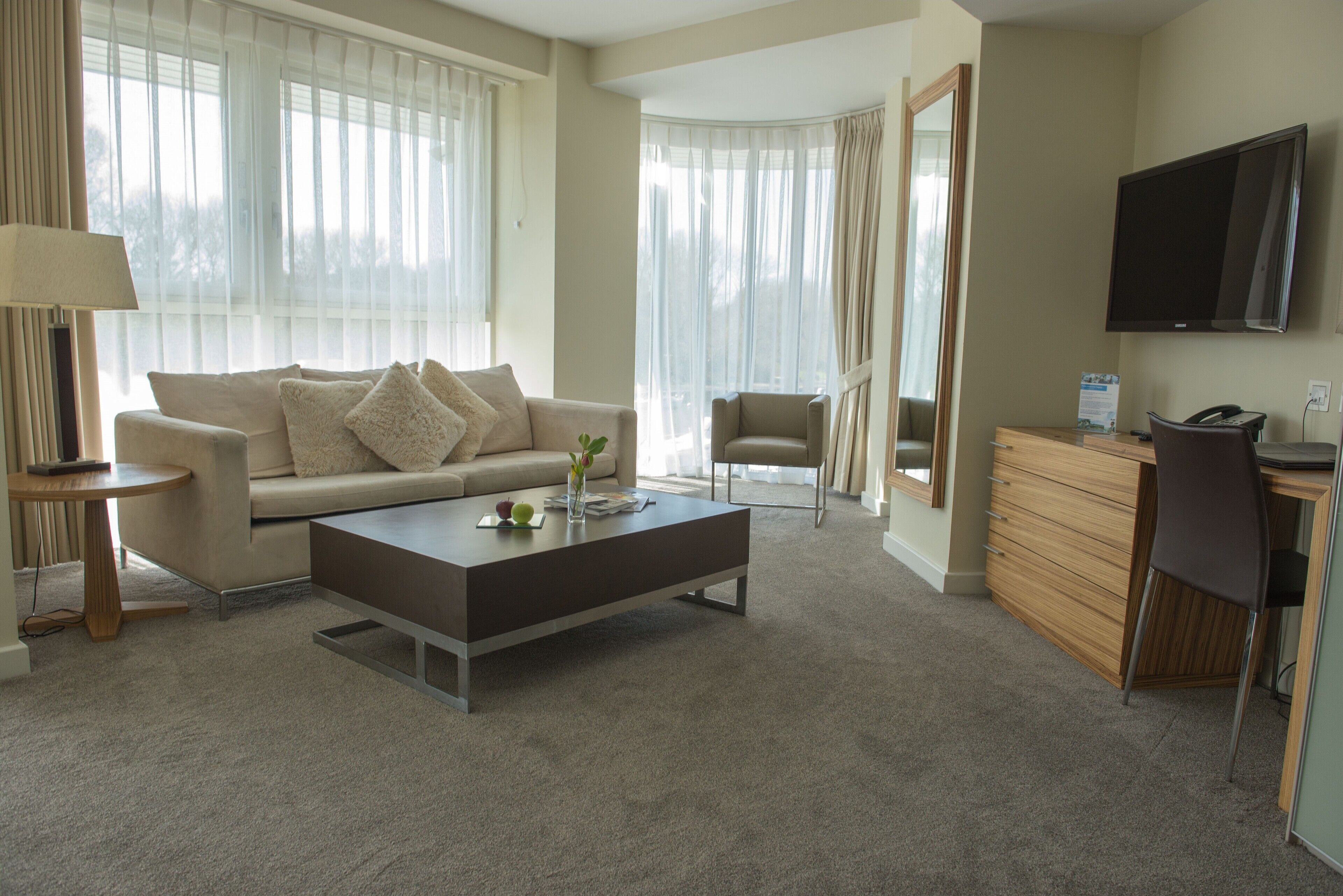 A modern hotel room with a sofa, a coffee table, a desk, and a TV.