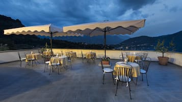 Eine Terrass mit Tischen, Stühlen, Sonnenschirmen und Topfpflanzen.