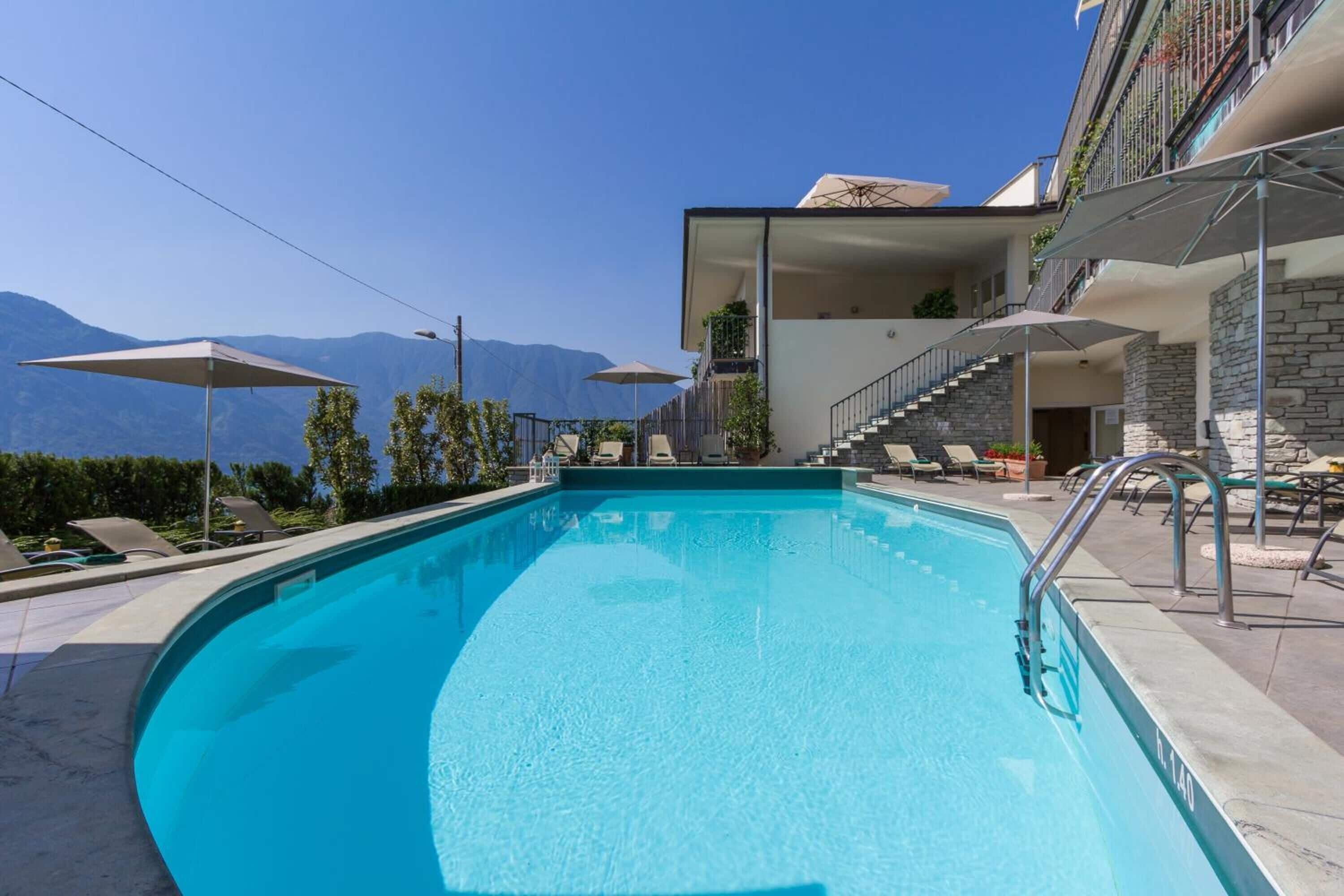 A swimming pool with a clear view of mountains, a covered outdoor seating area, and a staircase leading to an upper level.