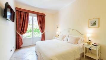 Quarto com cama, mesas de cabeceira, televisão e janela com cortinas.