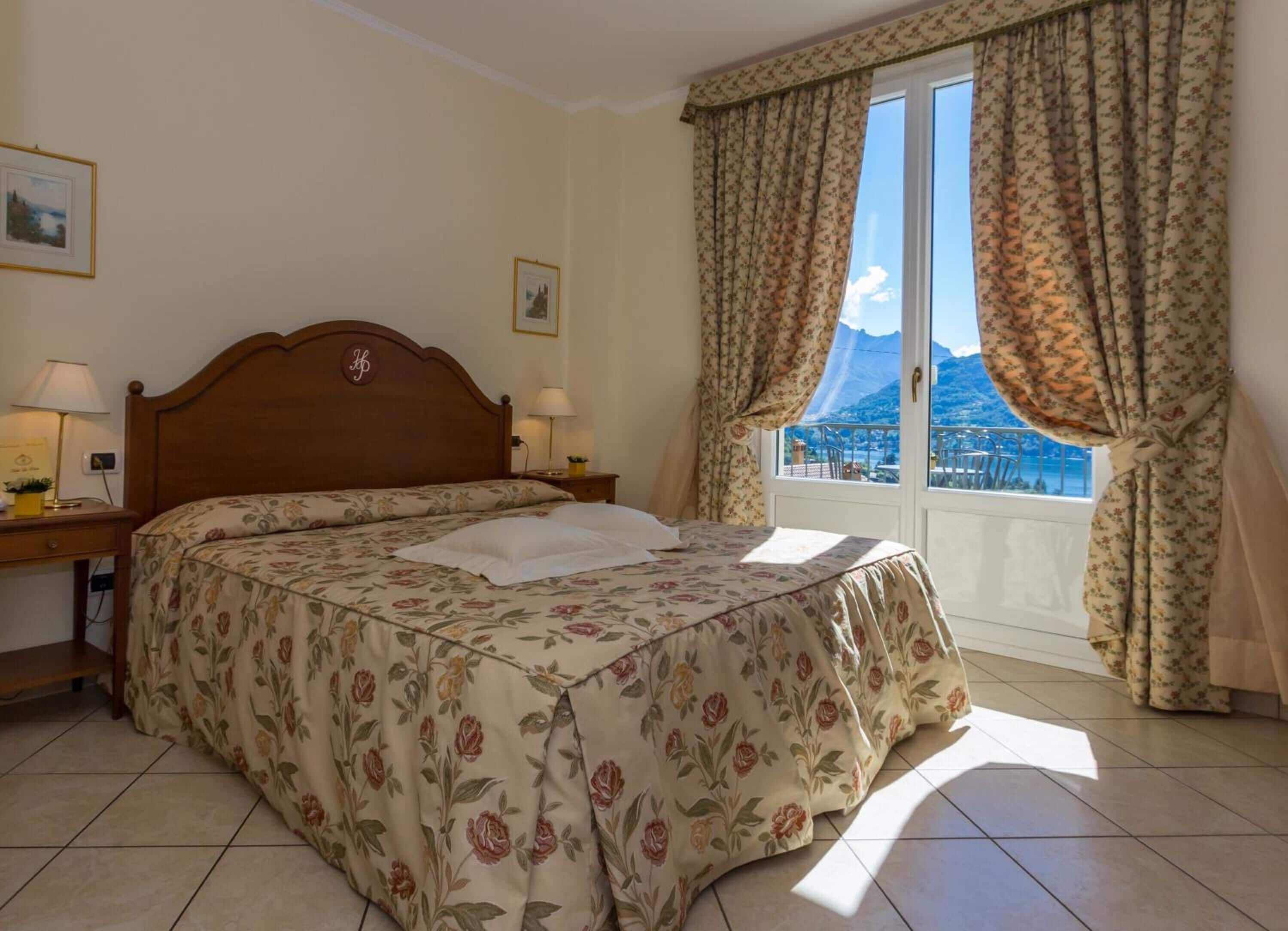 A bedroom with a bed, two bedside tables, a window with curtains, and a view of a mountain.