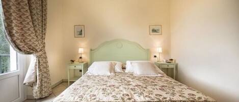 A room with a bed, two bedside tables, and a window with curtains.