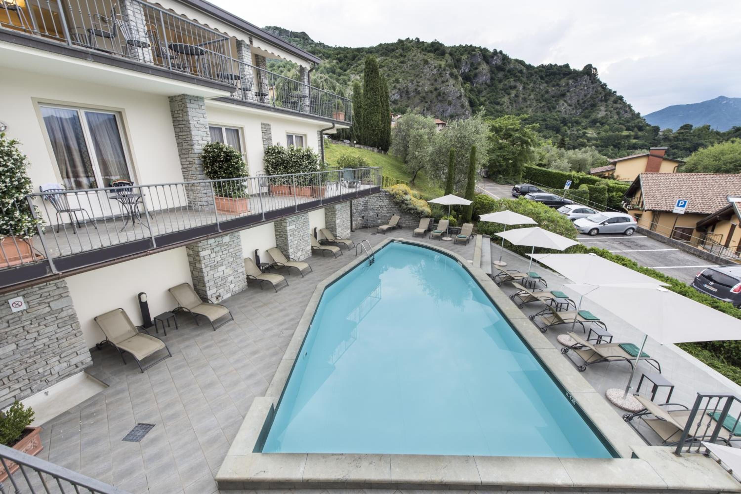 A swimming pool with lounge chairs and umbrellas, surrounded by a building with a stone facade and a balcony.