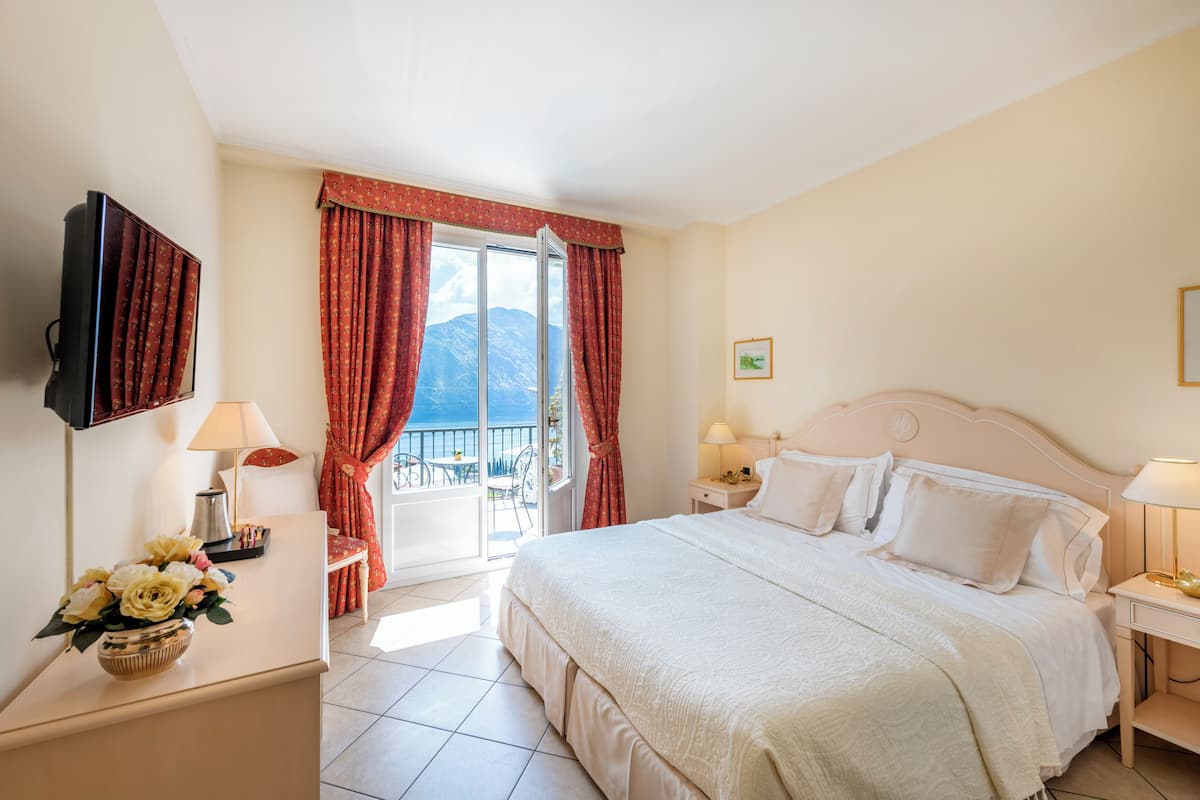 A hotel room with a bed, bedside tables, a TV, and a view of mountains through the window.
