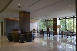 A spacious lobby with large vases, modern furniture, and large windows offering a view of greenery.