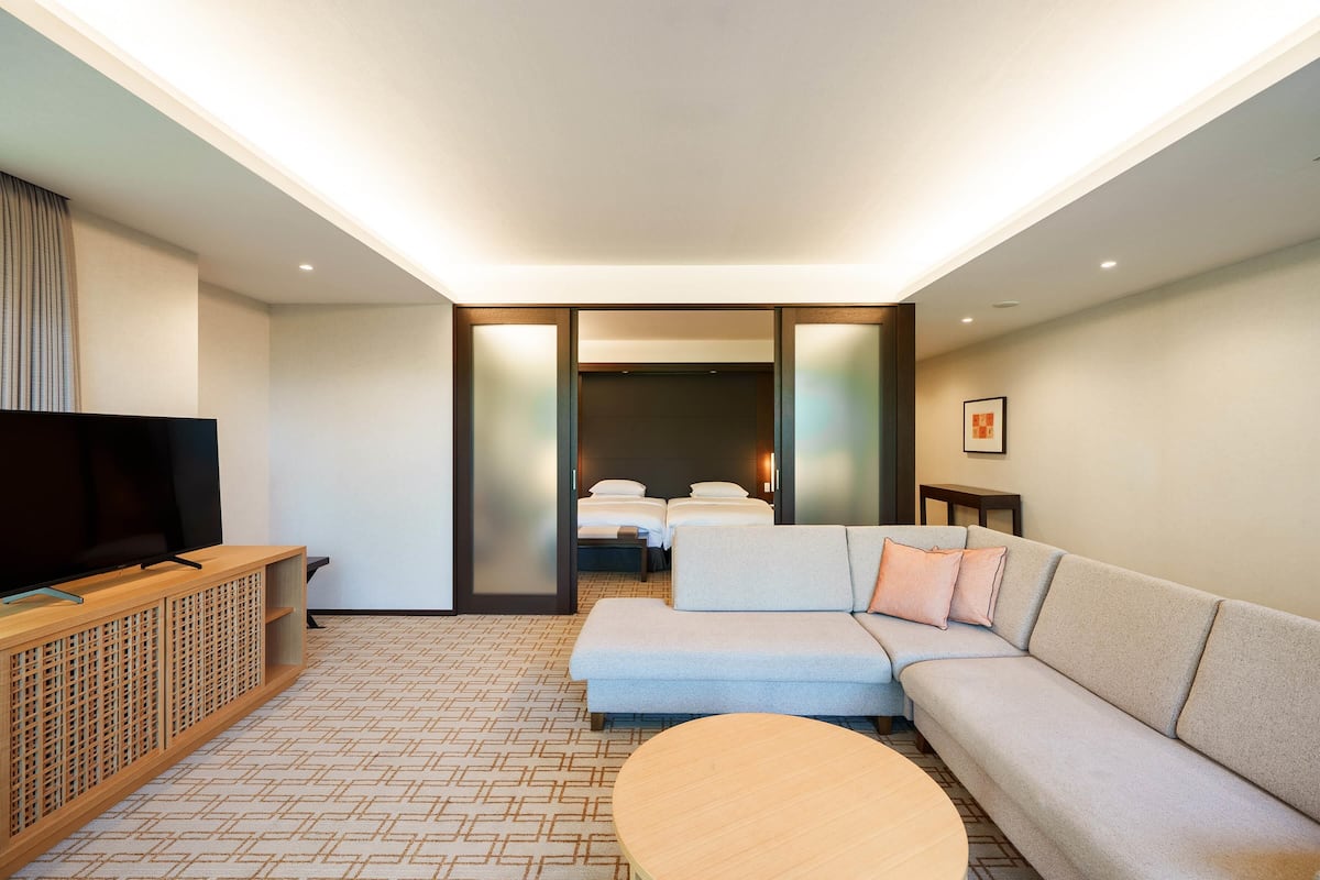 A modern hotel room with a sofa, a television, a small table, and a bed with two pillows.