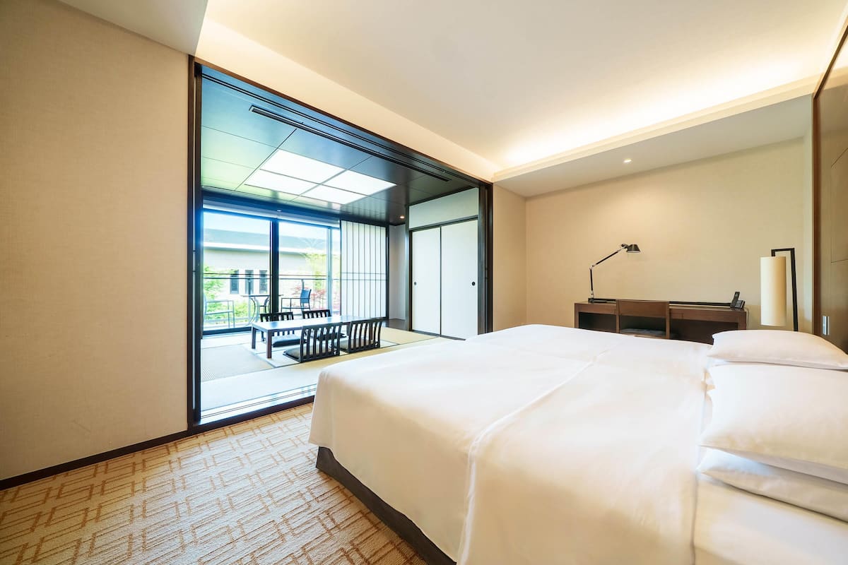 A modern hotel room with a large bed, a desk, and a view of an outdoor seating area.