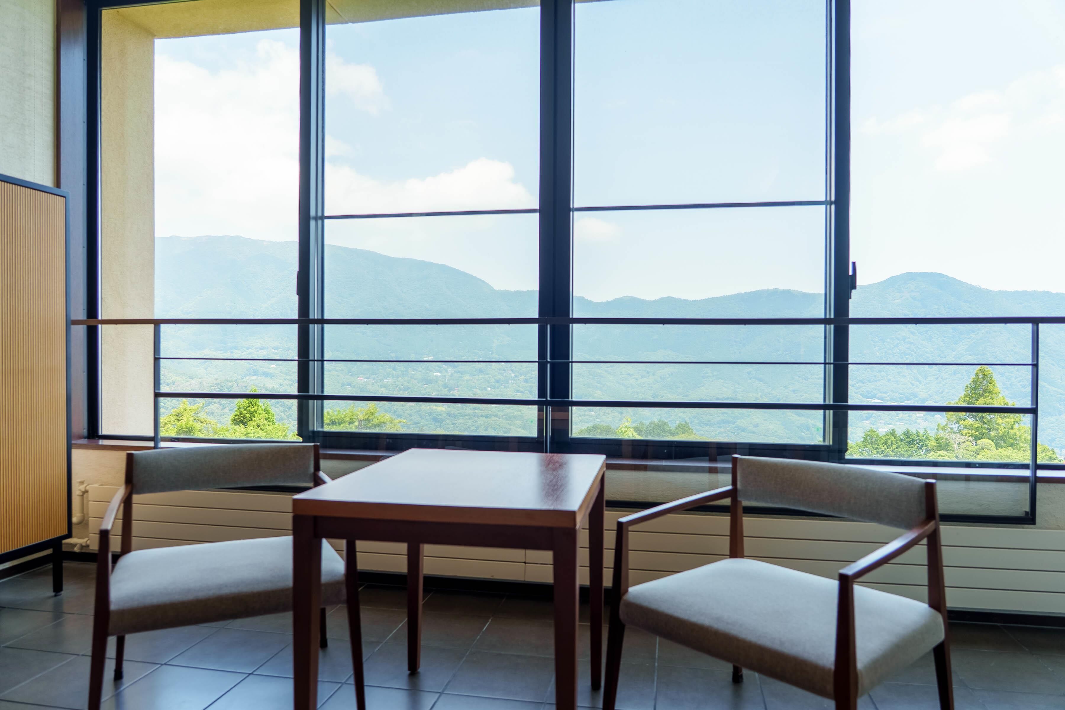 A room with a large window offering a mountain view, a wooden table, and two chairs.