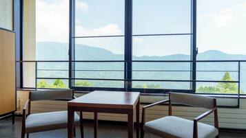 A room with a large window offering a mountain view, a wooden table, and two chairs.