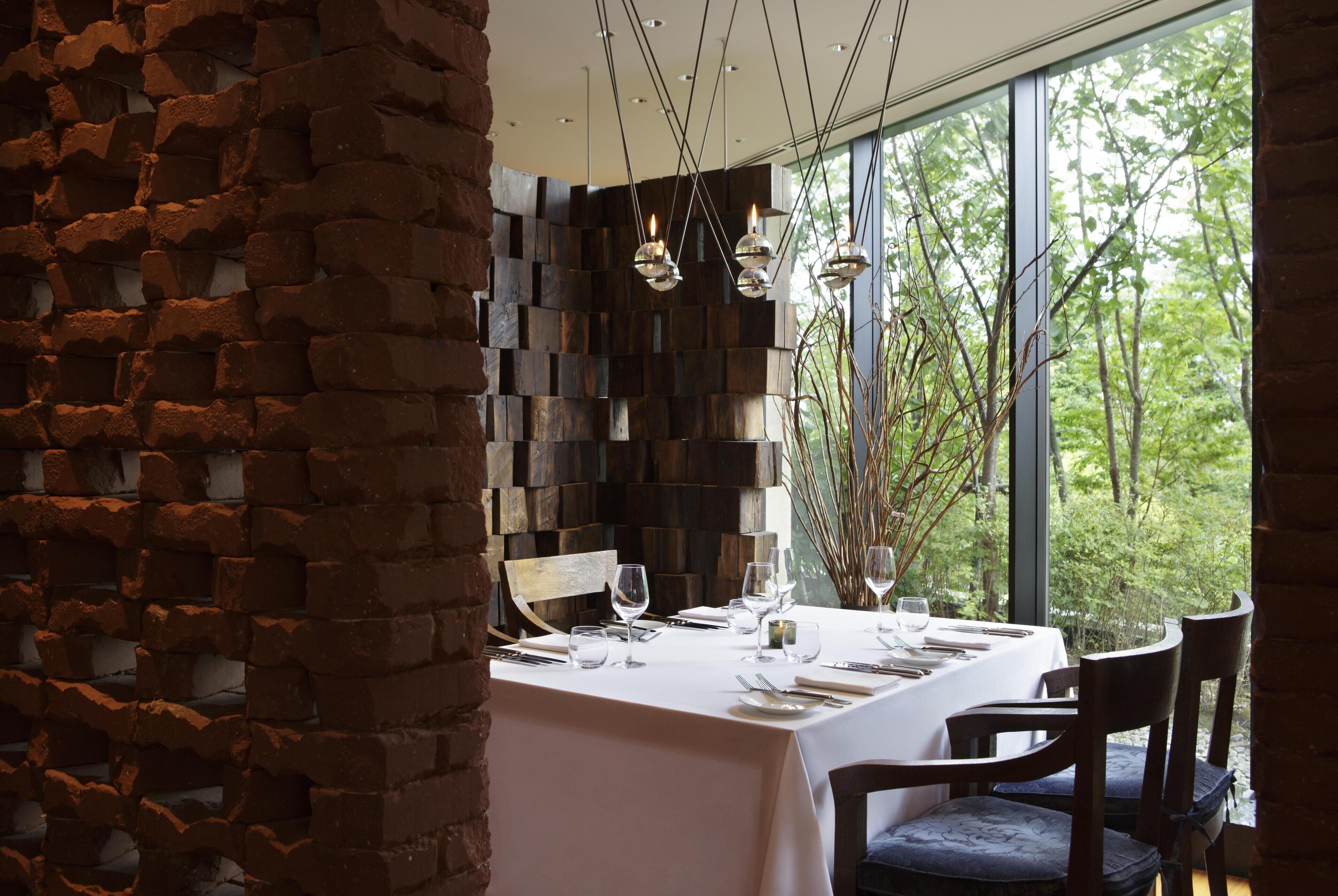 A dining area with a brick wall, a table set for four, and a view of greenery through large windows.