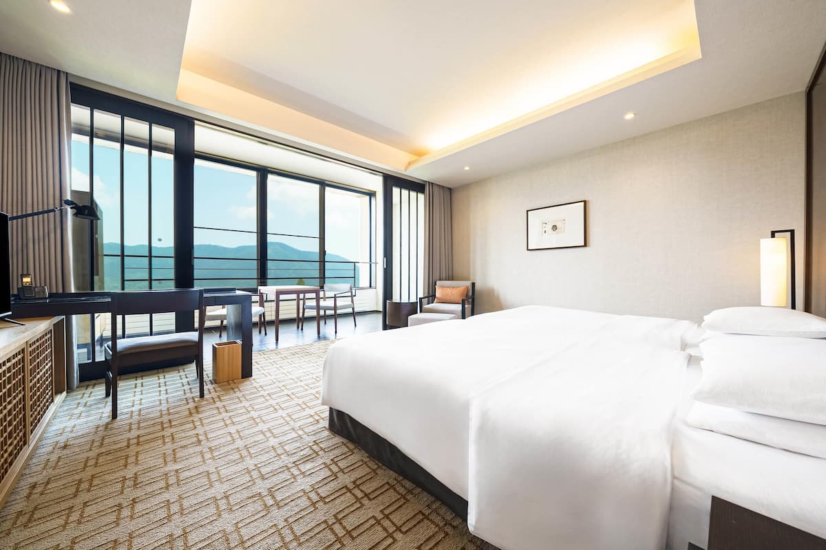 A hotel room with a large bed, a desk, and a view of the mountains through large windows.