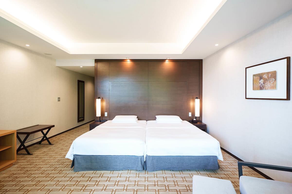 A hotel room with two beds, a desk, and a bench.