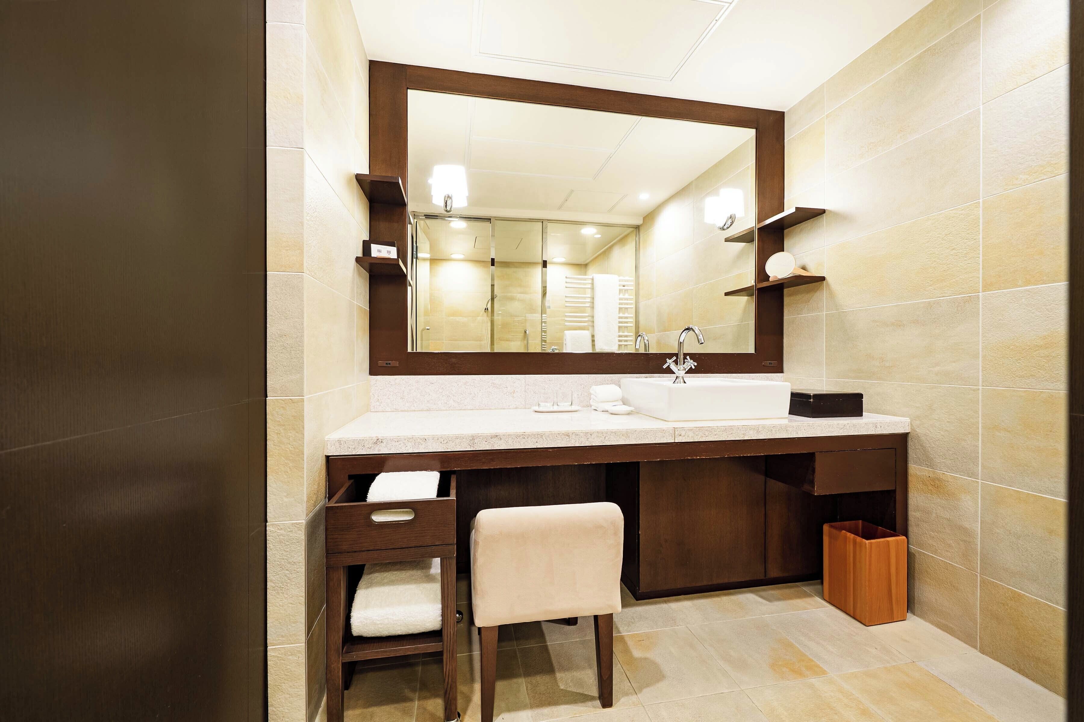 A modern bathroom with a large mirror, a sink, a towel rack, and a trash bin.