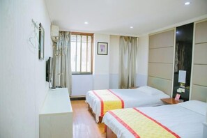 Quarto de hotel com duas camas, uma escrivaninha, janela com cortinas e televisão presa à parede.