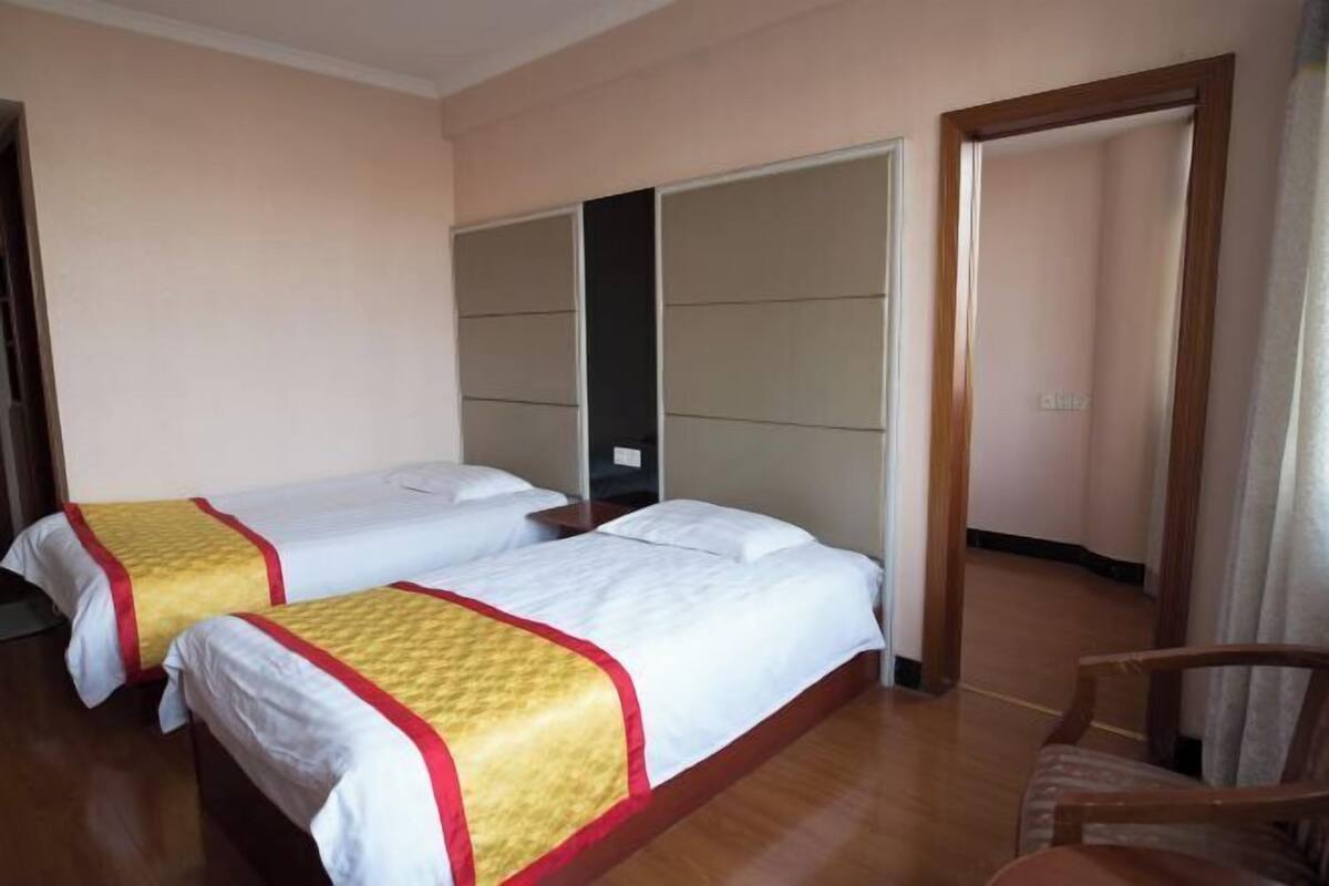 A hotel room with two beds, a wooden floor, a wooden chair, and a wardrobe.