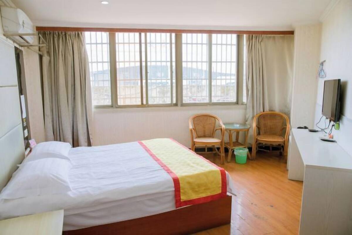 A hotel room with a bed, a desk, two chairs, a television, and a window with curtains.