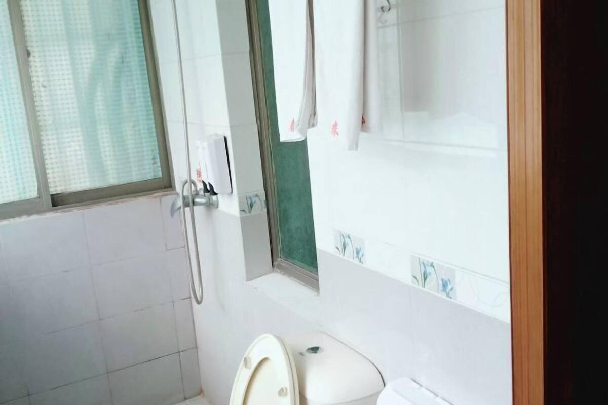 A bathroom with a toilet, a shower, and a window with a curtain.