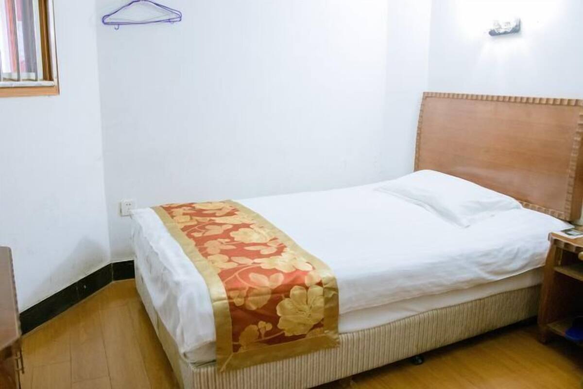 A single bed with a wooden headboard, a white bedspread, and a red floral blanket.