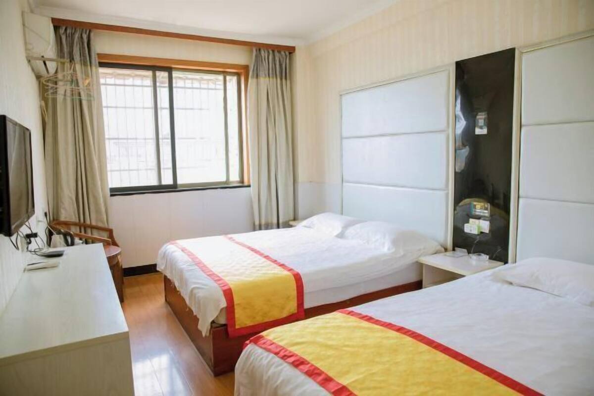 A hotel room with two beds, a desk, a chair, a window with curtains, and a wardrobe.