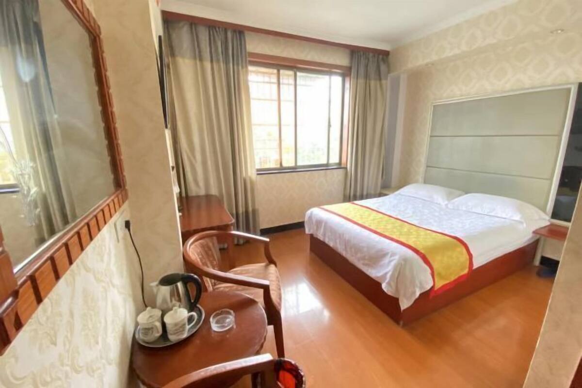 A hotel room with a bed, a desk with a chair, a coffee maker, and a window with curtains.