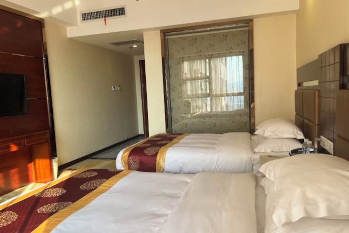 Una habitación de hotel con dos camas, cabecera de madera, televisor y ventana con cortinas.