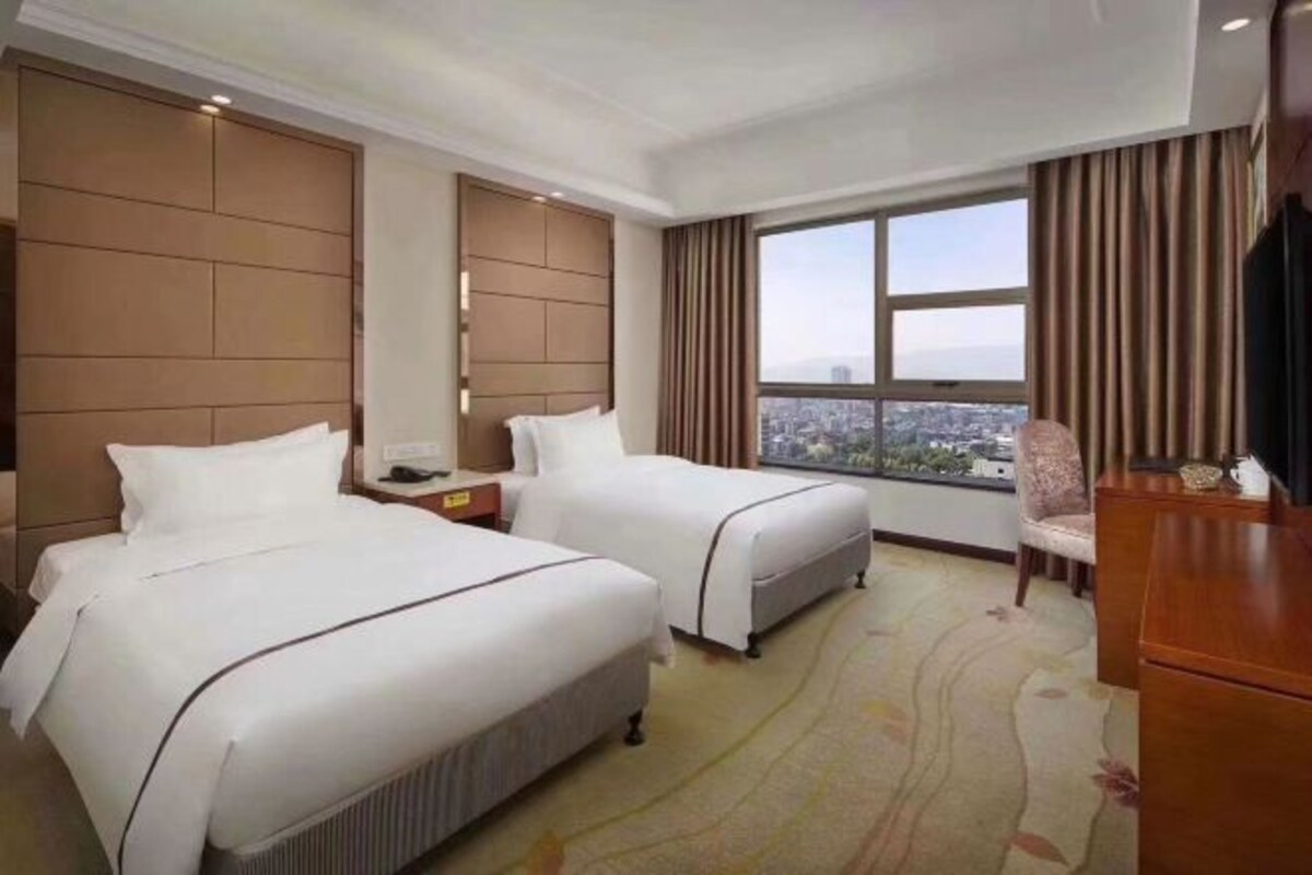 Habitación de hotel con dos camas, un amplio ventanal con vistas a la ciudad, un escritorio y una silla.