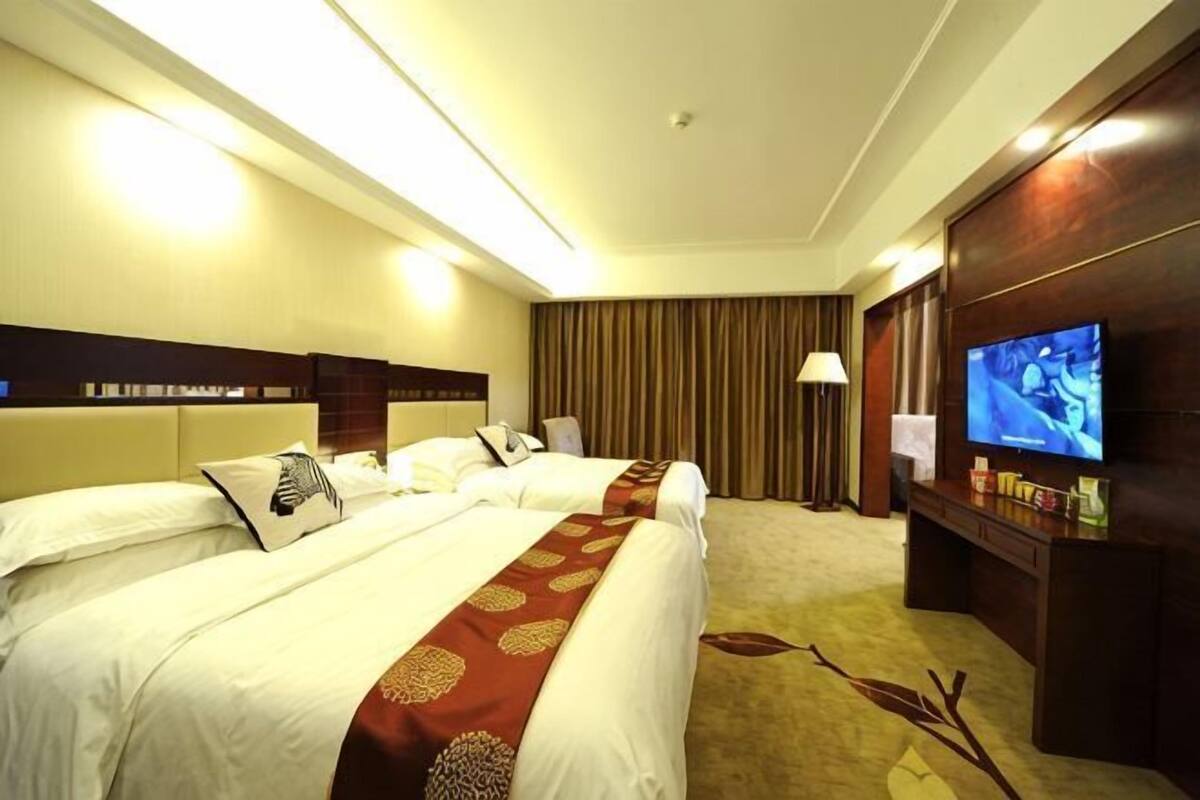 Habitación de hotel con dos camas, televisión, escritorio y un ventanal grande.