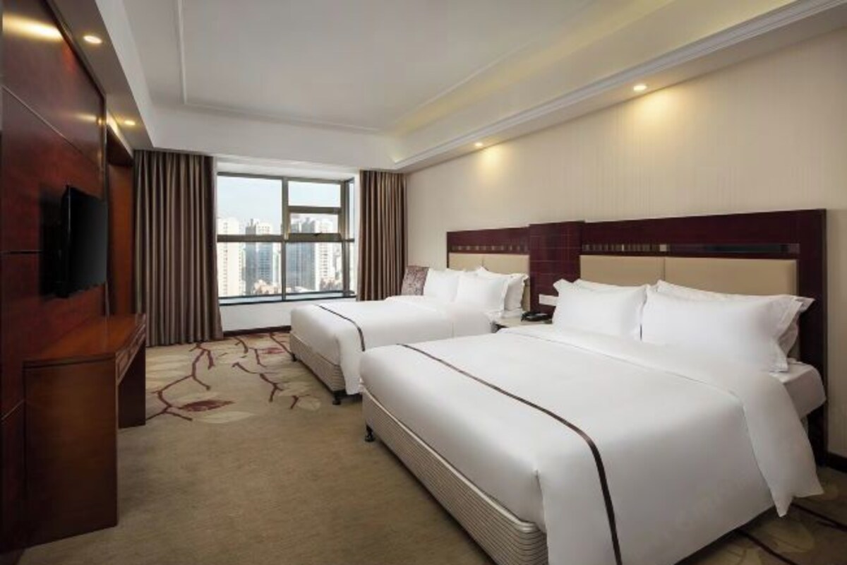 Habitación de hotel con dos camas, televisión, ventana grande y vista a la ciudad.