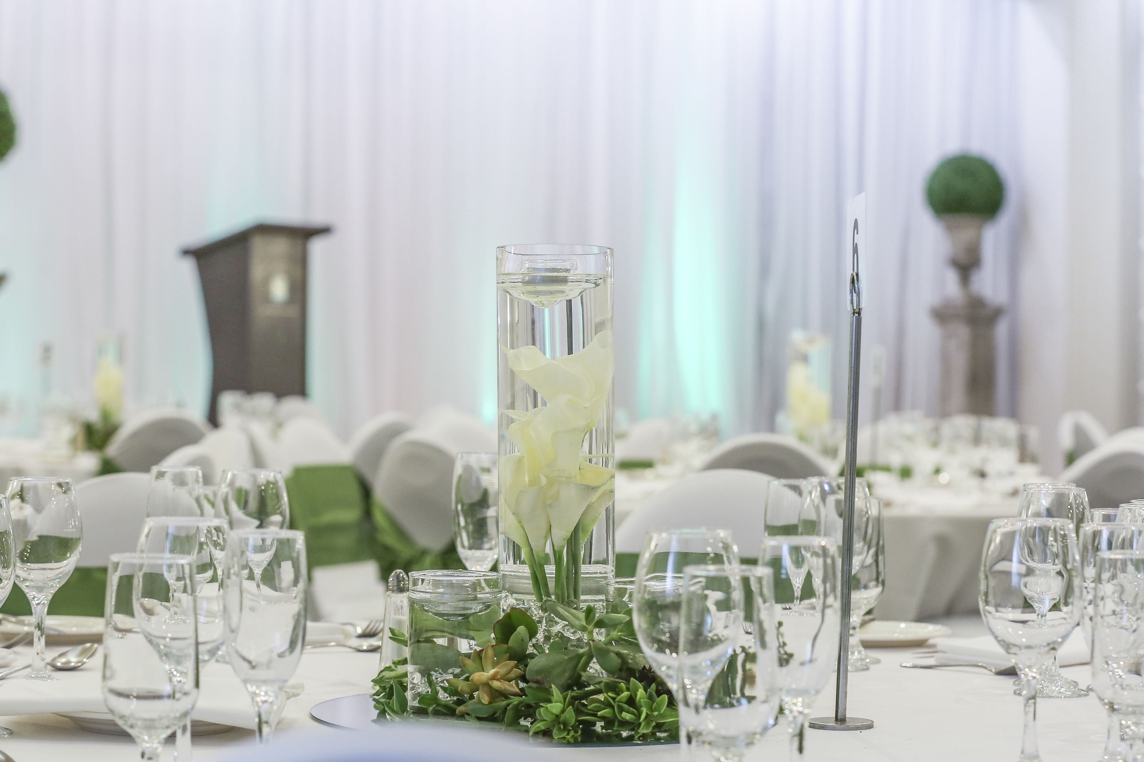 A table set for a formal event with clear glassware, a tall glass with white flowers, and a candle holder.