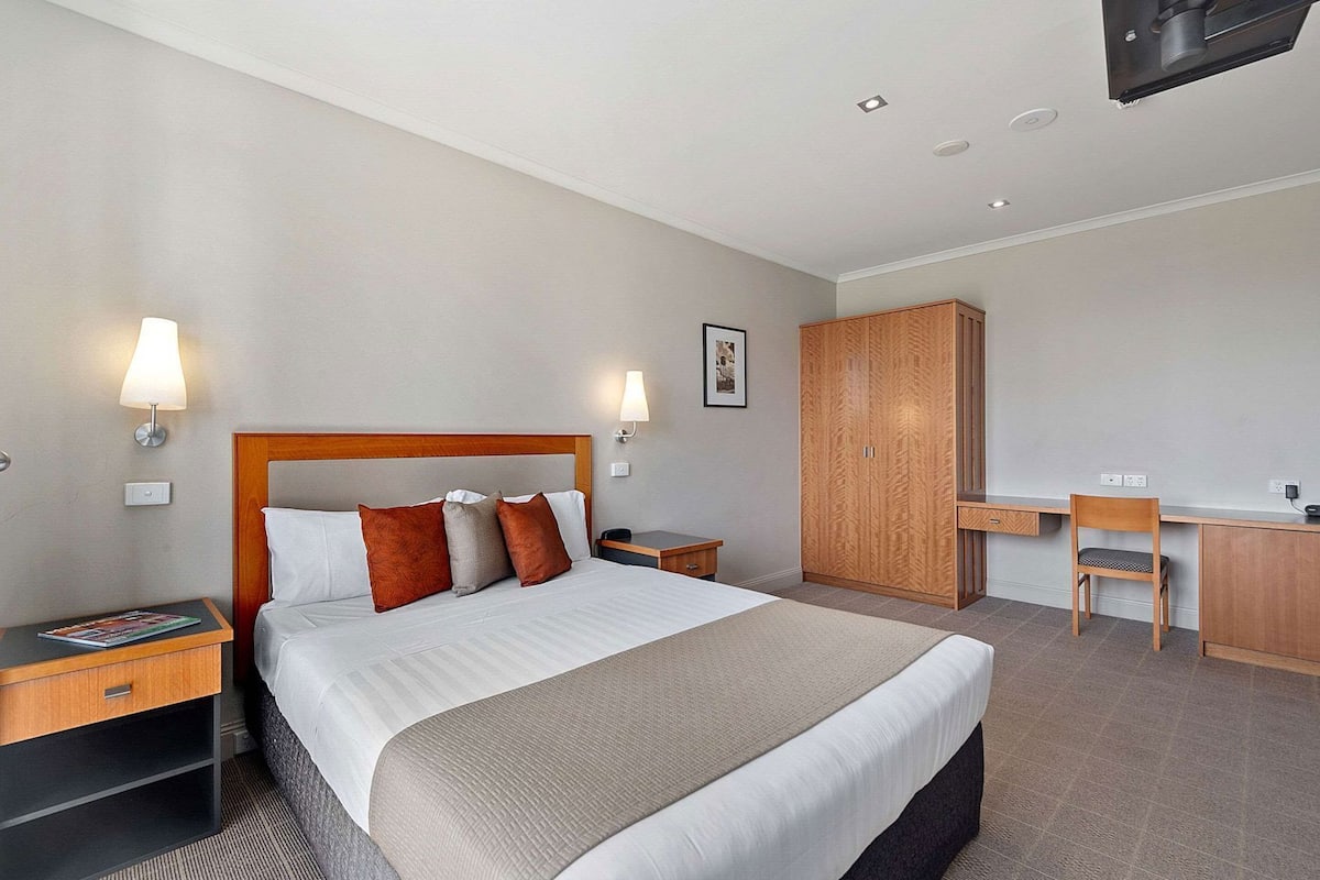 Une chambre d’hôtel comprenant un lit, des tables de chevet, un bureau, une chaise, une armoire et un téléviseur fixé au mur.
