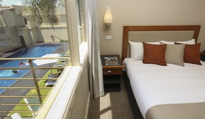 Une chambre d’hôtel avec un lit, une table de chevet, une lampe et une vue sur une piscine.