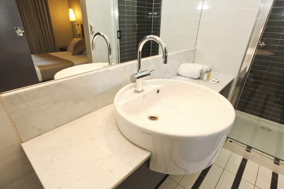 Ein Badezimmer mit einem weißen Waschbecken, einem Spiegel, einer Dusche und einem Handtuch auf der Ablagefläche.
